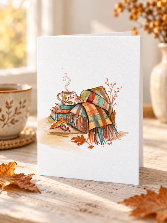 Tea, books, and patchwork blankets greeting card in a cozy autumn tabletop scene