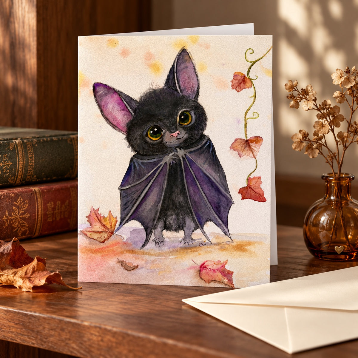 Batinsky greeting card standing on a wooden shelf beside books, an amber vase and an envelope.