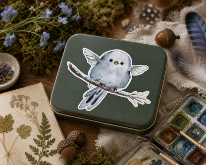 Blue Fairy Nestling vinyl sticker on a keepsake art-supply tin with botanical accents