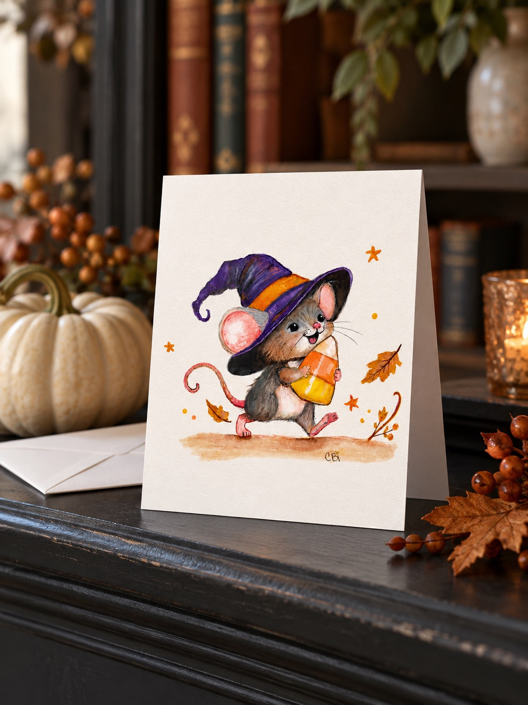 Candy Corn Mischief greeting card on a dark mantel beside a white envelope and cream pumpkin.