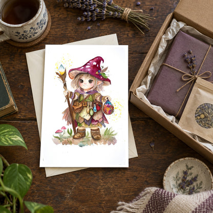 Little Cottage Witch greeting card beside an envelope and a care package with a wrapped book and tea. Gifting scene; props are not included.