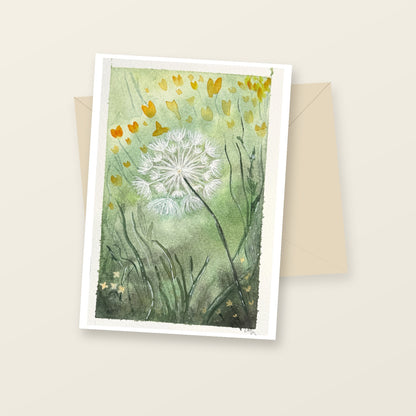 Dandelion blank greeting card laid flat with a cream envelope, featuring the original green and yellow watercolor artwork and artist’s signature.