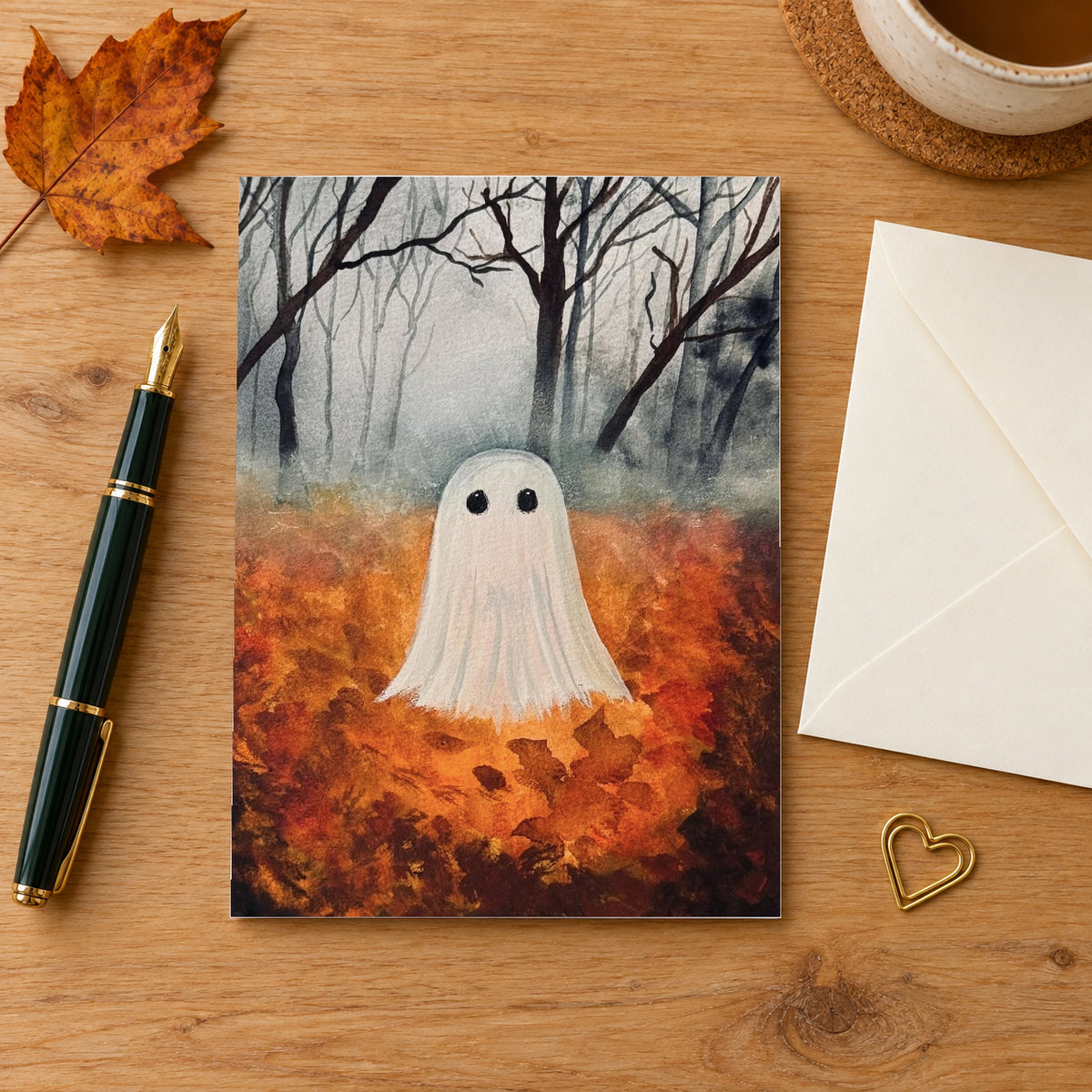 Fall Ghost greeting card on a wooden writing desk beside an envelope, fountain pen and autumn leaf.