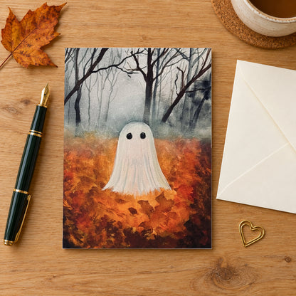Fall Ghost greeting card on a wooden writing desk beside an envelope, fountain pen and autumn leaf.