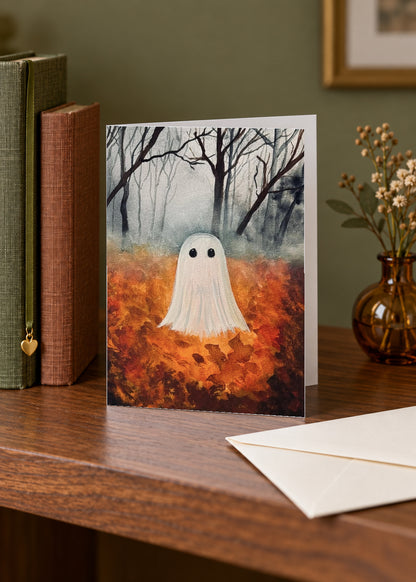 Fall Ghost side-fold greeting card standing on a walnut shelf beside books, an amber vase and an envelope.