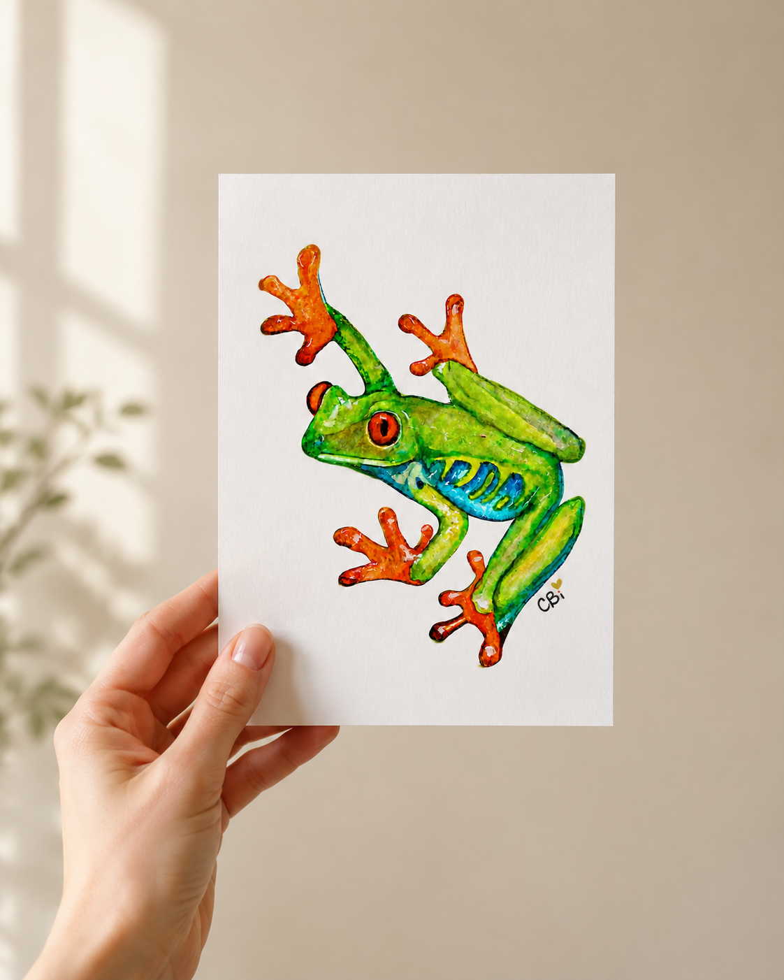 Red-Eyed Frog greeting card in an artist’s flat lay with the green watercolor frog and pond reflection visible.