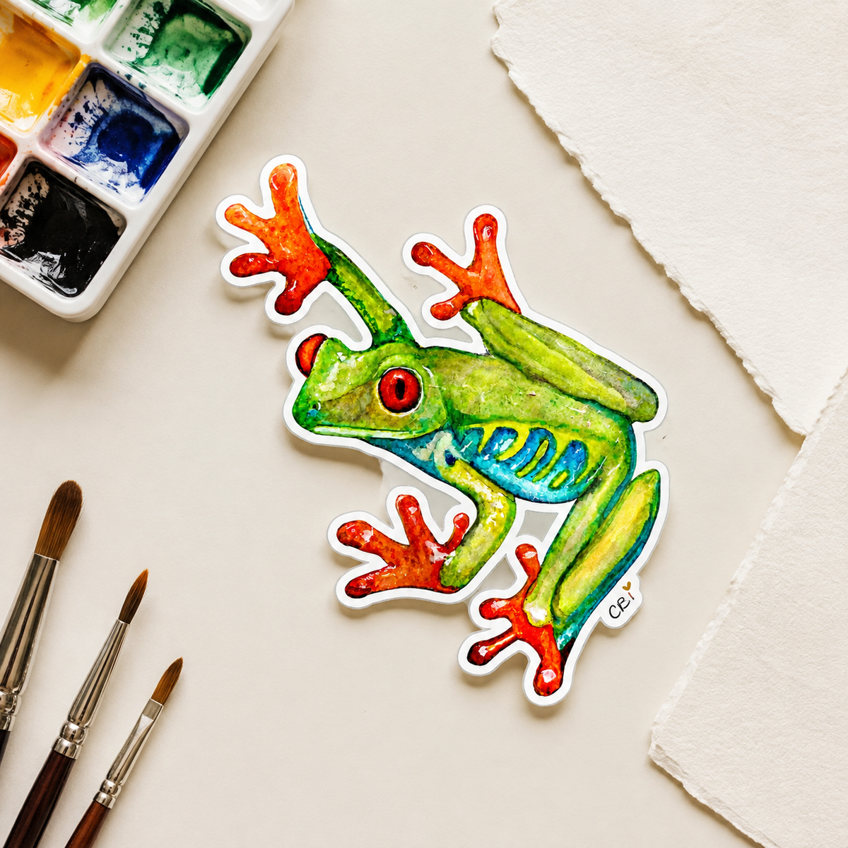 Red-eyed frog sticker in an artist studio flatlay
