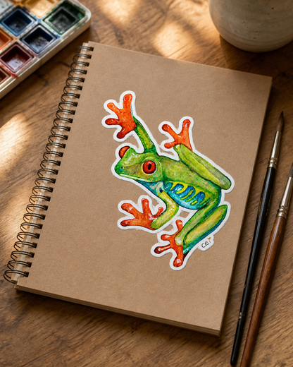 Red-eyed frog sticker on a watercolor sketchbook