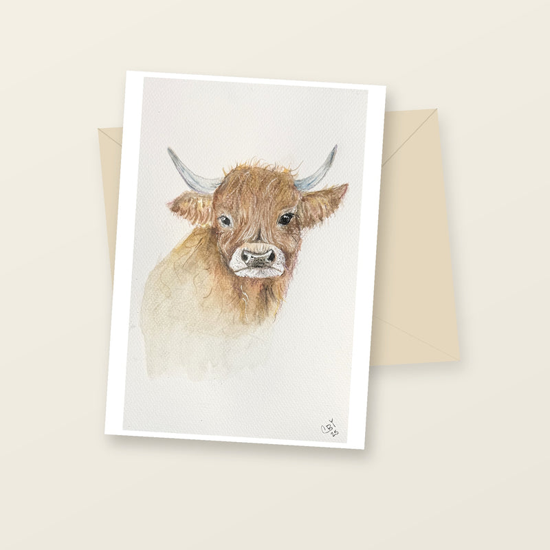 Highland cow greeting card laid flat beside a cream envelope.