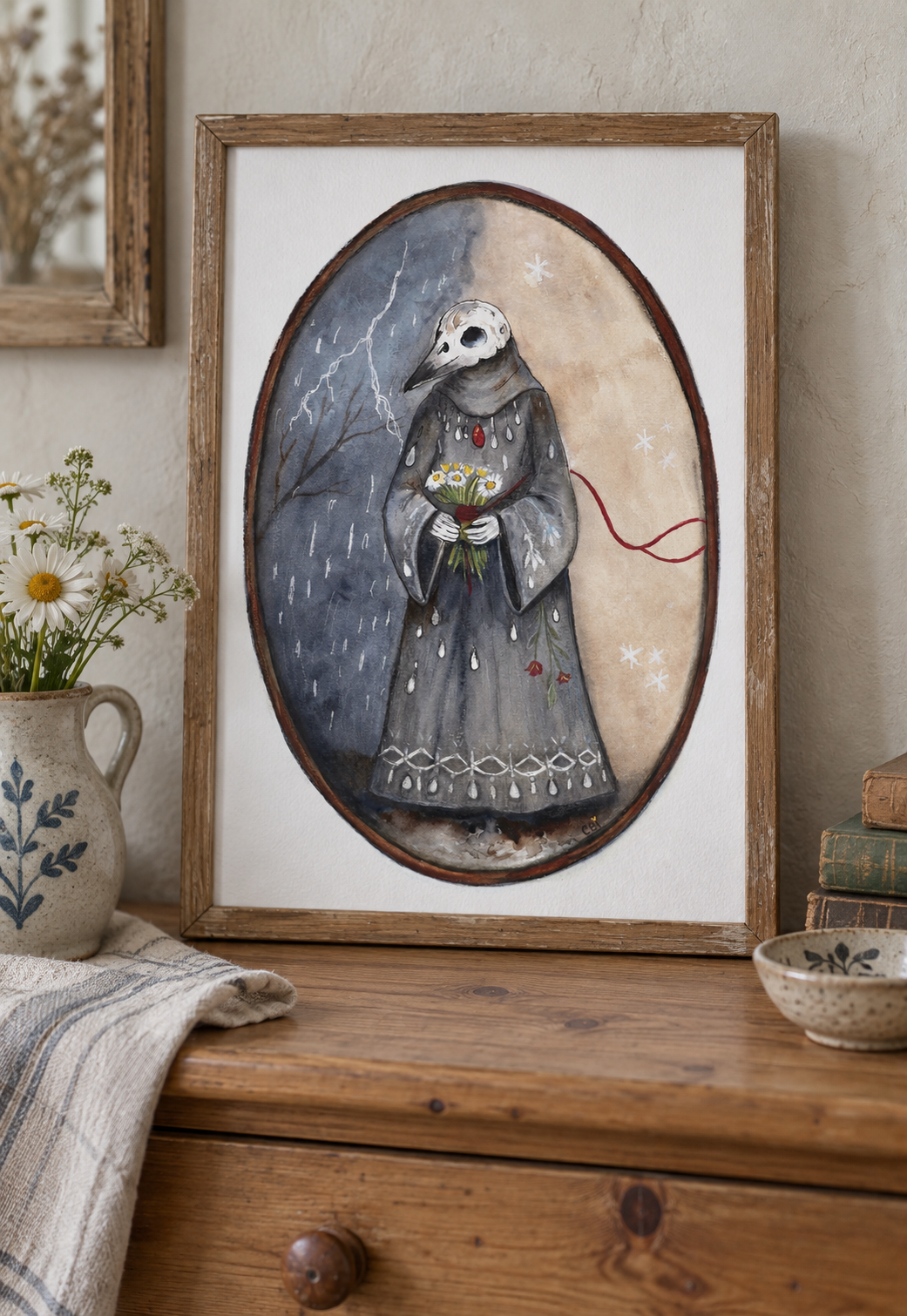 The Keeper Between Seasons print in a natural wood frame on a cottage dresser beside daisies.