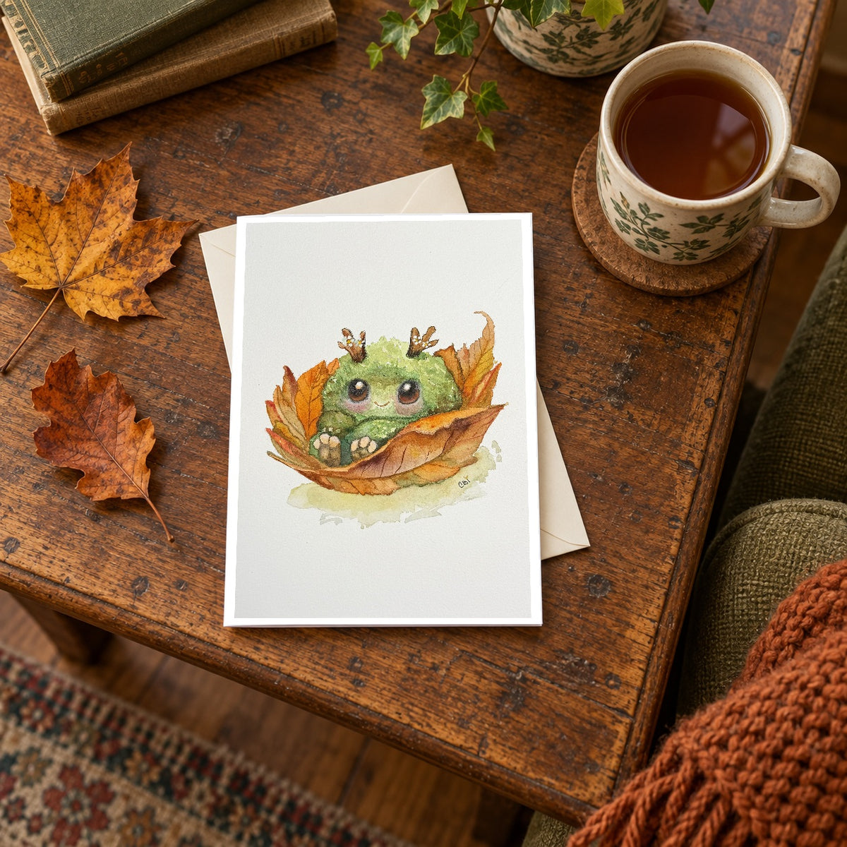 Fall Mossling greeting card on an autumn reading table beside tea, books and fallen leaves.