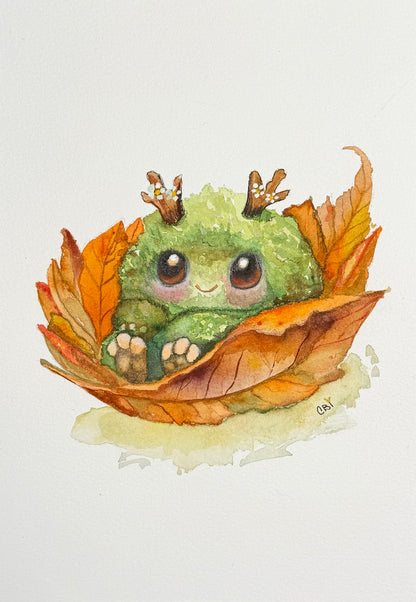 Complete original watercolor of a small green creature with twig antlers nestled in orange leaves, including the artist’s signature.