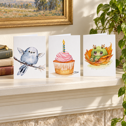 Blue Fairy Nestling, Birthday Cupcake, and Fall Mossling greeting cards standing on a cream mantel.